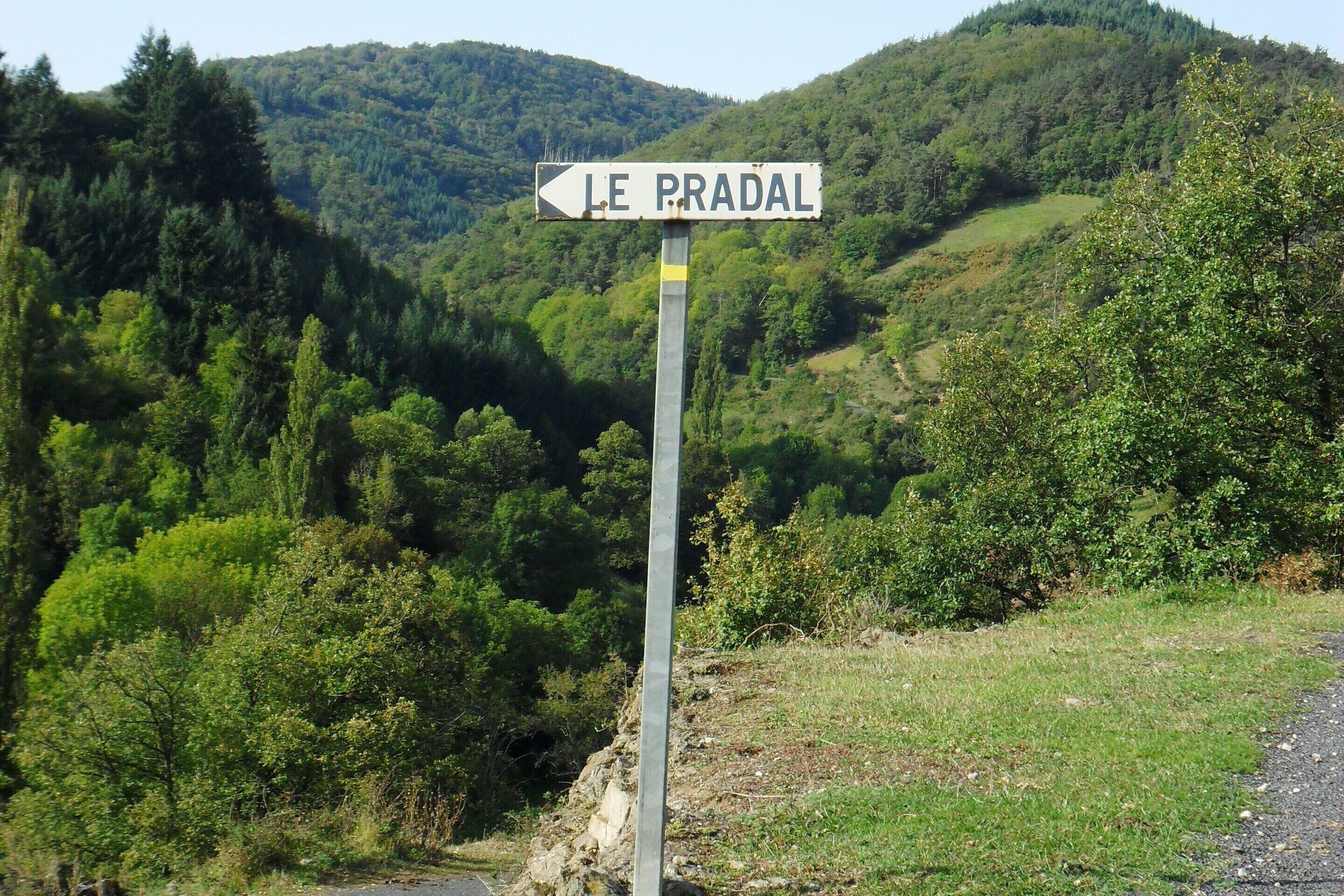 Un panneau indicateur portant l’inscription « LE PRADAL », placé sur un fond de paysage vallonné et de végétation luxuriante.