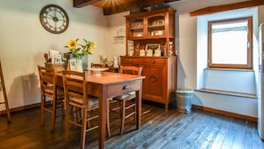 A wooden dining table with chairs, a wooden cabinet with glassware, a clock, and a window with a view. - Hideaway in Villeneuve-d'allier (Ally)