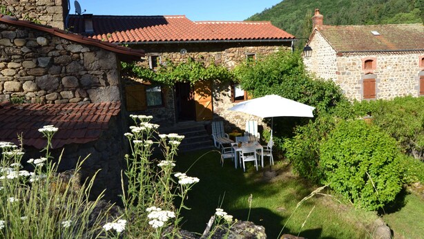 A stone building with a red-tiled roof, a patio with outdoor furniture, and a garden with white flowers. - Hideaway in Villeneuve-d'allier (Ally)