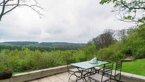 A patio with a table and chairs overlooking a forested landscape.