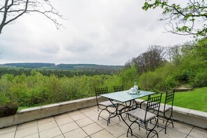 A patio with a table and chairs overlooking a forested landscape.