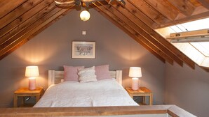 A cozy attic bedroom with a sloped ceiling, a chandelier, a bed with patterned pillows, and two bedside lamps.