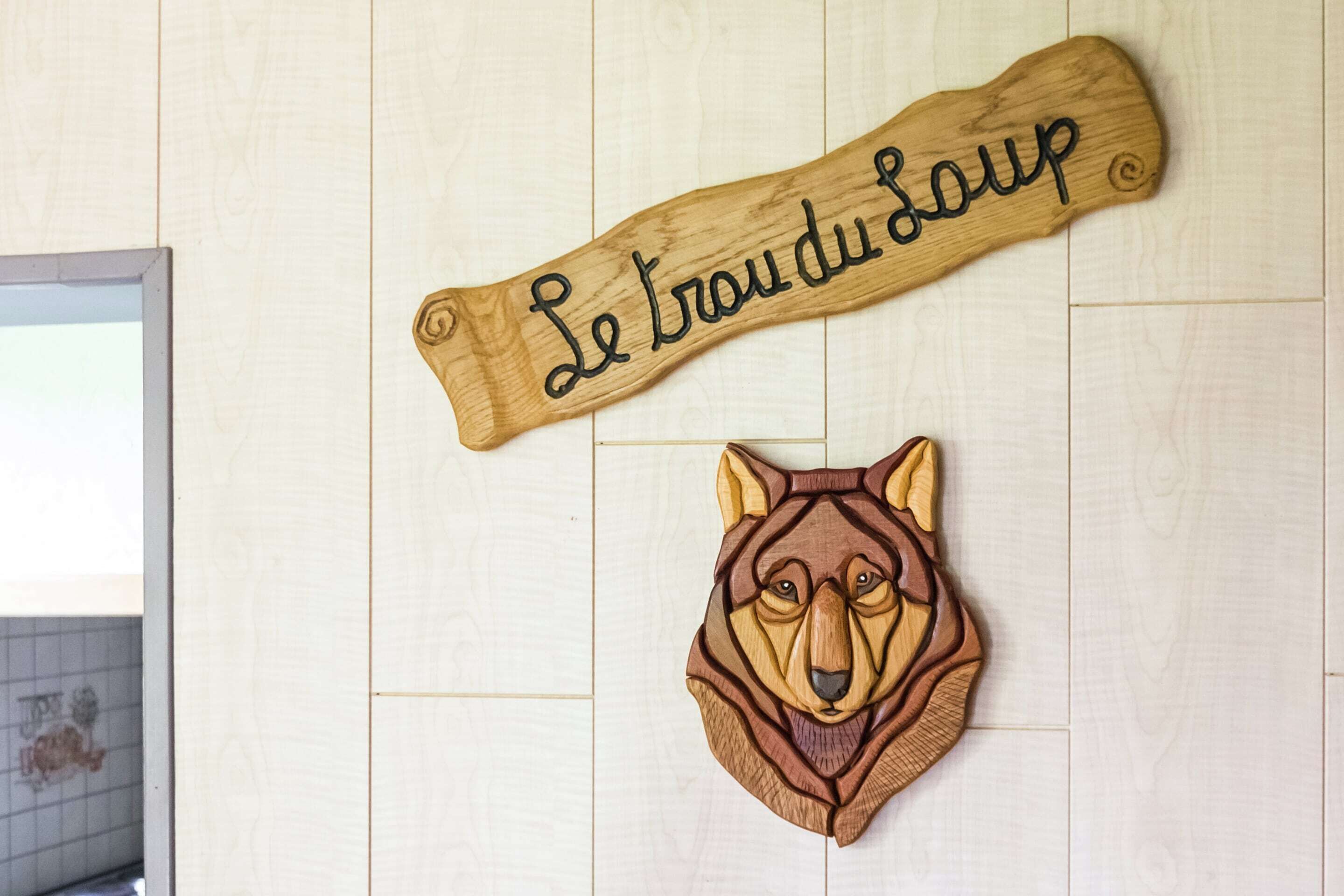 A wooden sign with carved text and a fox head decoration on a tiled wall.