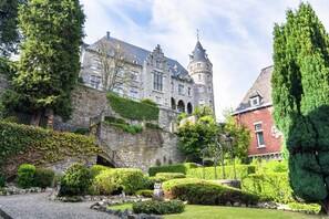 A historic building with a turret, stone walls, and a well-maintained garden with hedges and trees. - Perfect Spot on Edge of Large Woods with Hot Tub (Saint-Hubert)