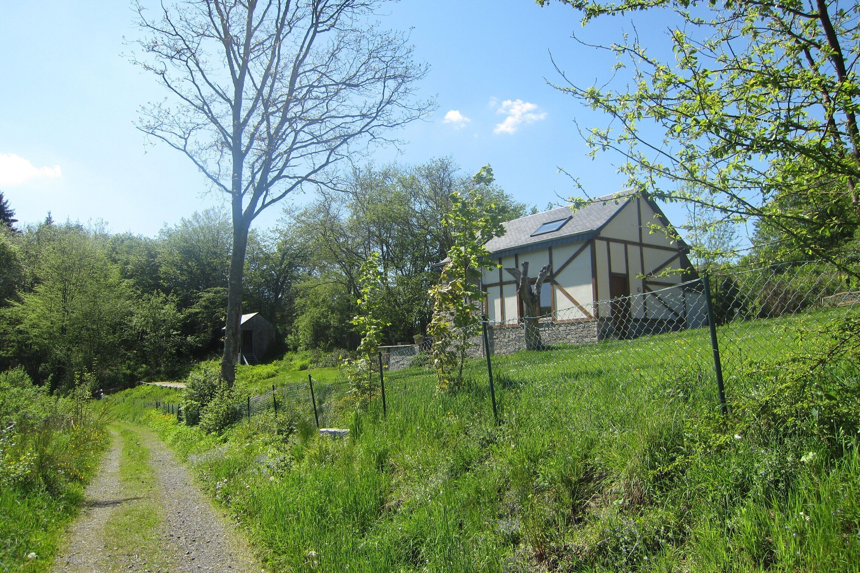 A house with a sloped roof and a stone foundation, surrounded by a grassy area and trees.
