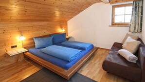 A wooden-paneled room with a bed, a nightstand, a reading lamp, a brown sofa, and a window with curtains. - Apartment in Kaltenbach Near Ski Lift (Kaltenbach)