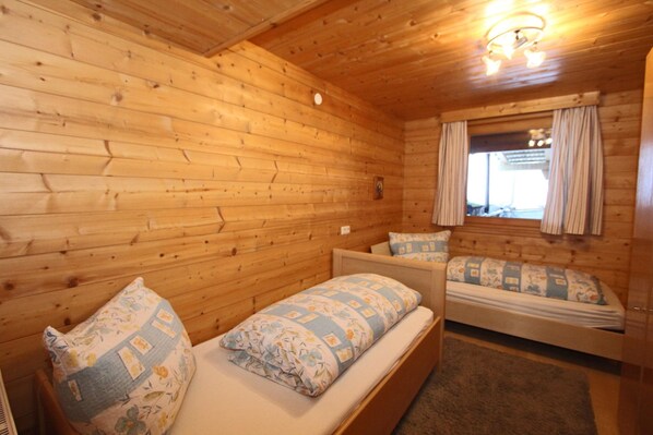 A wooden cabin room with two beds, a window with curtains, and a ceiling light.