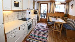 A compact kitchen with white cabinets, a stove, and a dining area with a bench and table. - Apartment in Kaltenbach Near Ski Lift (Kaltenbach)