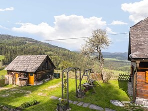 Situated in a lush valley, this cabin features a cozy porch with a wooden bench and a metal ladder leading to a swing set.