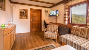 A cozy room with wooden floors, a wooden door, a television, a striped sofa, and a window with a view of trees. - Chalet in Kalchberg Near Klippitztorl Ski (Bad Sankt Leonhard im Lavanttal)