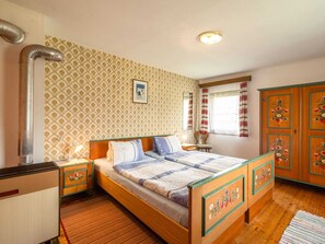 Classic hotel room with a wooden bed, nightstands, and a wardrobe, set against a patterned wallpaper backdrop.