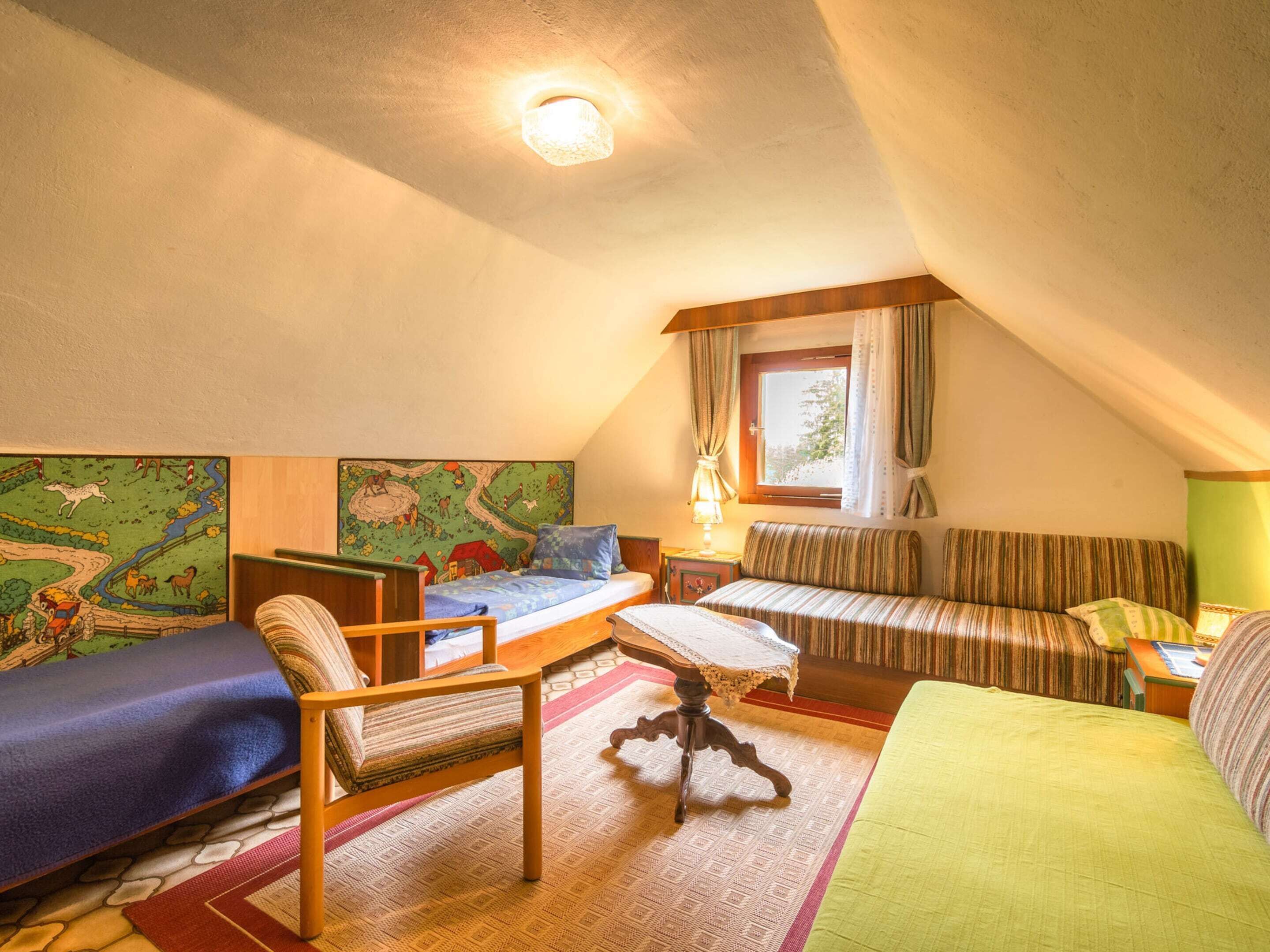 A cozy attic bedroom with a bunk bed, a single bed, a wooden chair, a patterned rug, and a window with curtains.