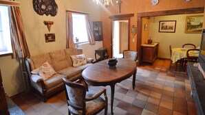Ein traditionelles Wohnzimmer mit Sofa, Esstisch und Stühlen. Eine Chandelier, ein Kamin und ein Gemälde an der Wand sind zu sehen.