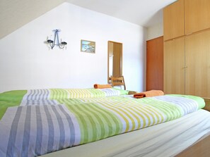 A bedroom with a bed, a wooden wardrobe, a mirror, and a wall-mounted light fixture.