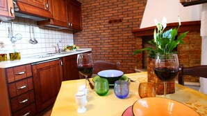 A kitchen with wooden cabinets, a brick wall, and a dining area with a table set for two. - Romantic Hideaway in Lazio (Selci)