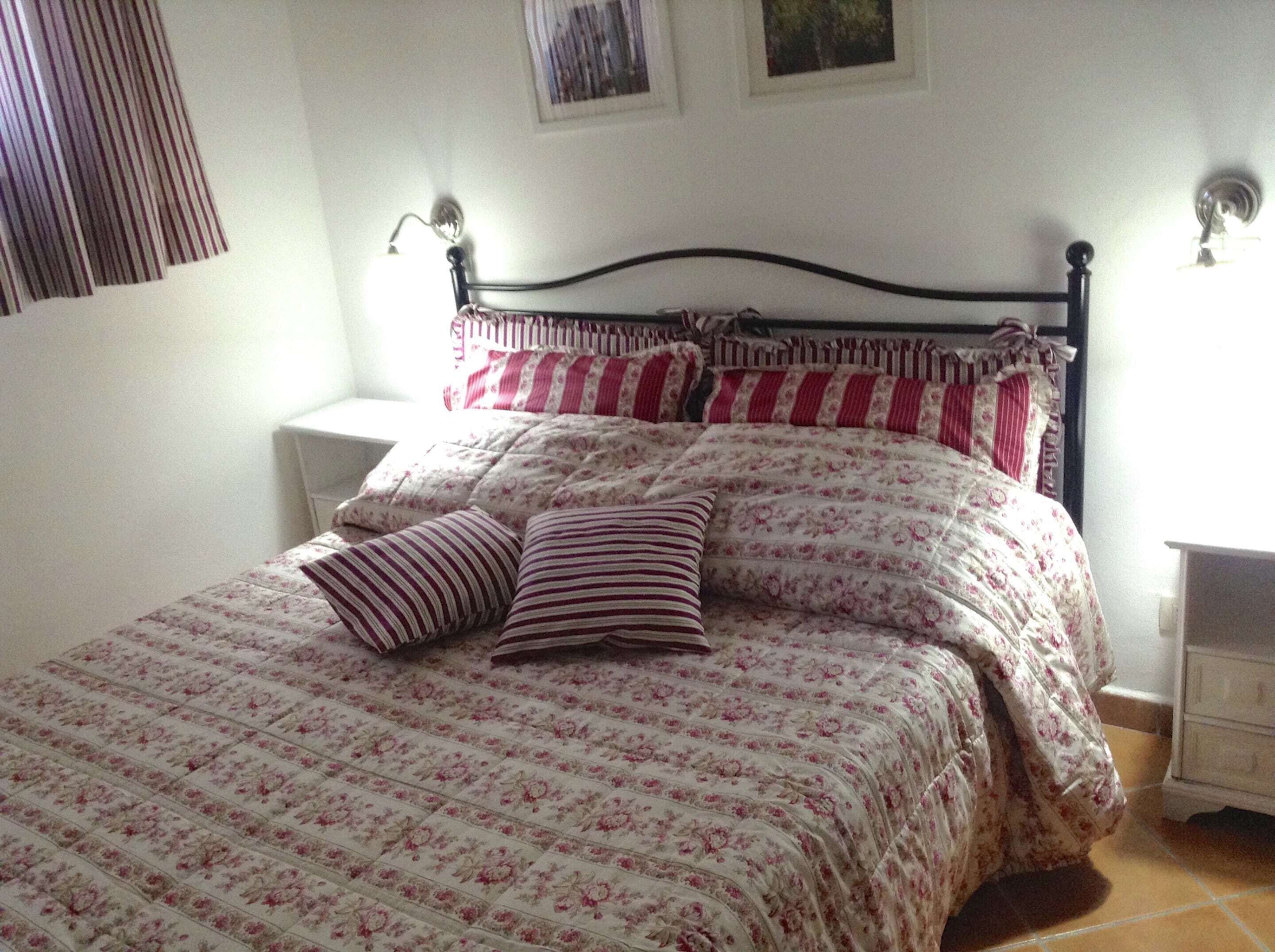 A bed with floral bedding and striped pillows, a nightstand, and a wall-mounted lamp.