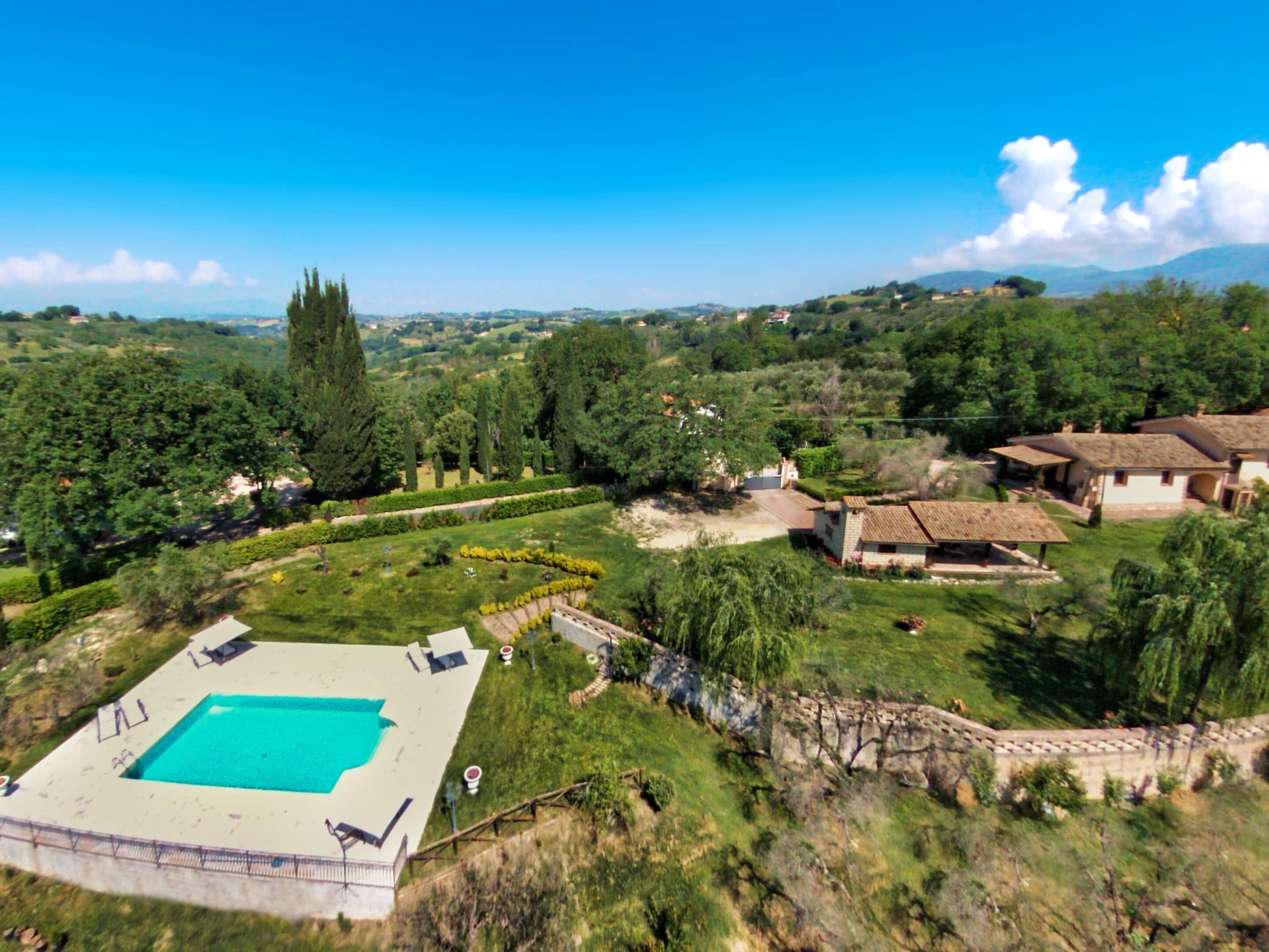 A large swimming pool with a surrounding deck, surrounded by lush greenery and traditional buildings.