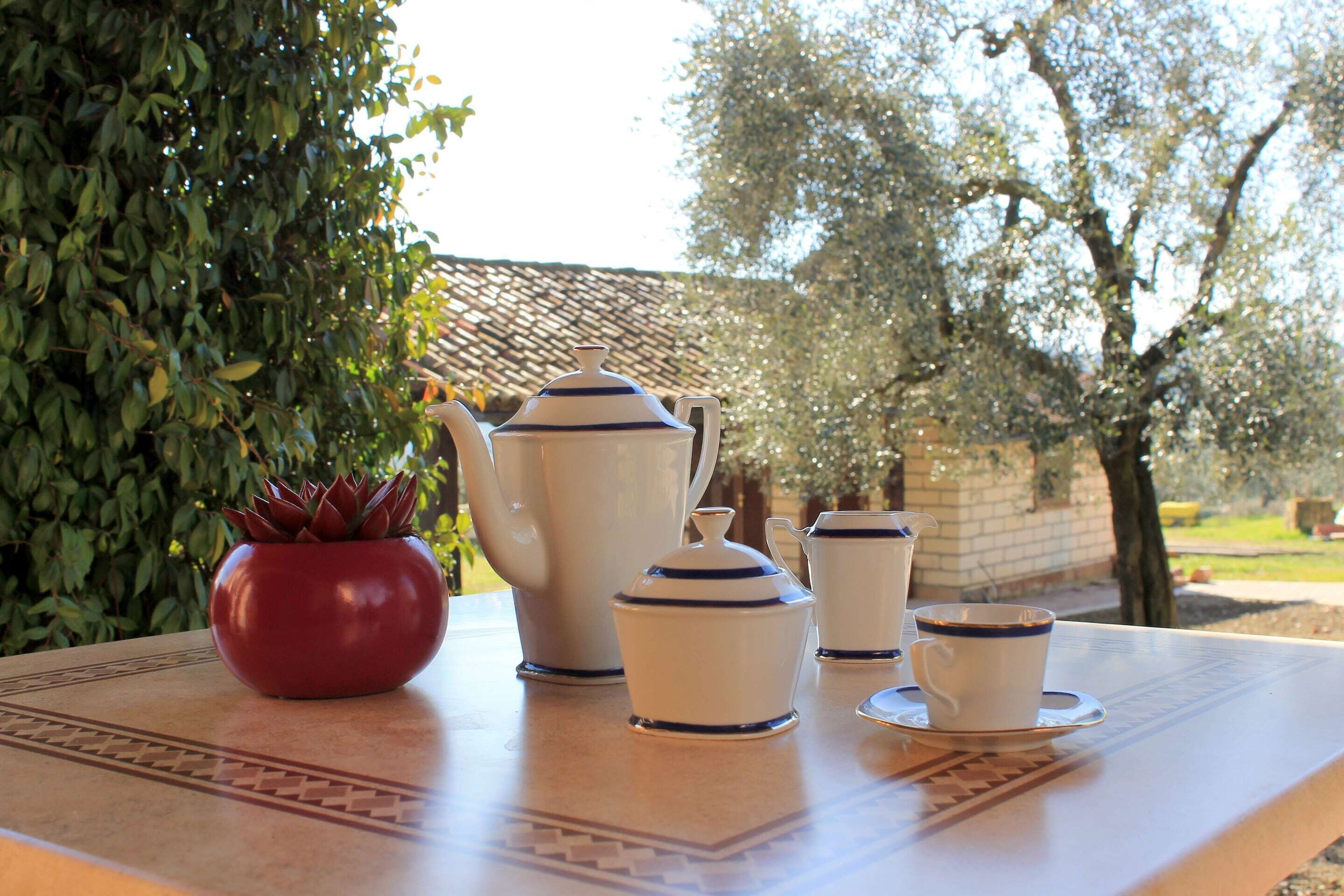 Een tafel met een servies van wit keramiek, inclusief een theepot, kopje en schoteltje, geplaatst op een tafelkleed met dessin.