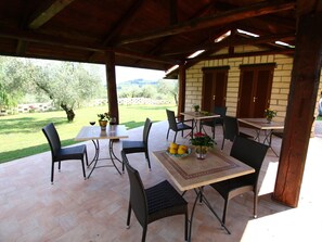 An outdoor patio with a wooden table and chairs, surrounded by a brick wall and a view of a garden and mountains. - Romantic Hideaway in Lazio (Selci)