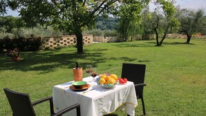 An outdoor dining table set with a bottle, glasses, and fruit under a tree. - Romantic Hideaway in Lazio (Selci)