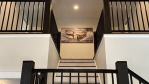 Un escalier orné d’un lustre, doté de rampes noires et surmonté d’un tableau représentant des bateaux.