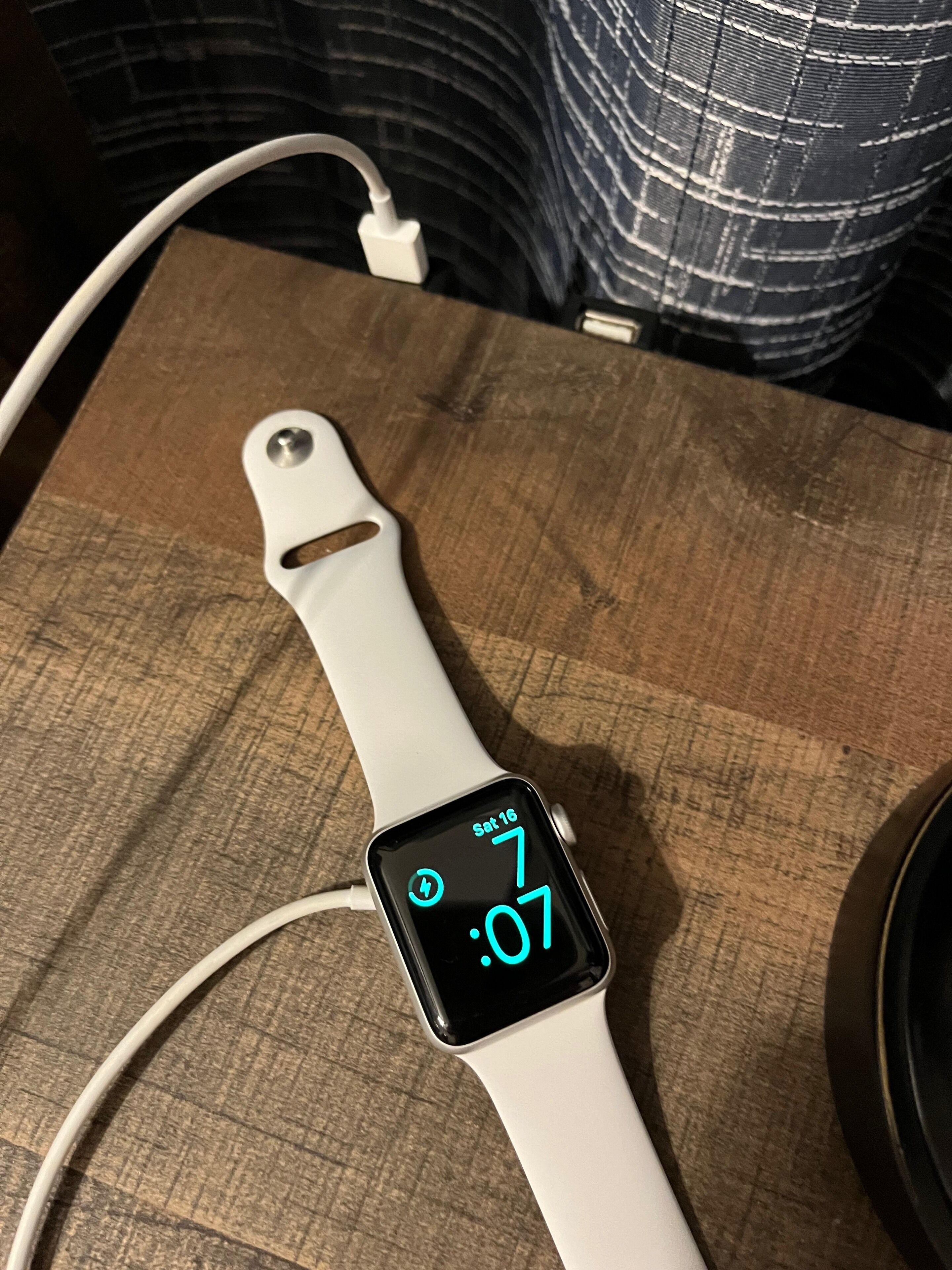 Une montre connectée posée sur une surface en bois, avec un bracelet blanc et un écran noir affichant l’heure et la date.