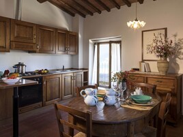 A kitchen with wooden cabinets, a dining table with chairs, a stove, and a window with a view.