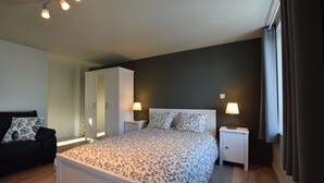 Une chambre à coucher comprenant un lit, des tables de chevet, une armoire, une commode, une lampe et une fenêtre avec des rideaux.