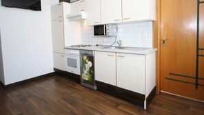 Een kleine keuken met witte kastjes, een magnetron, een fornuis en een vaatwasser.