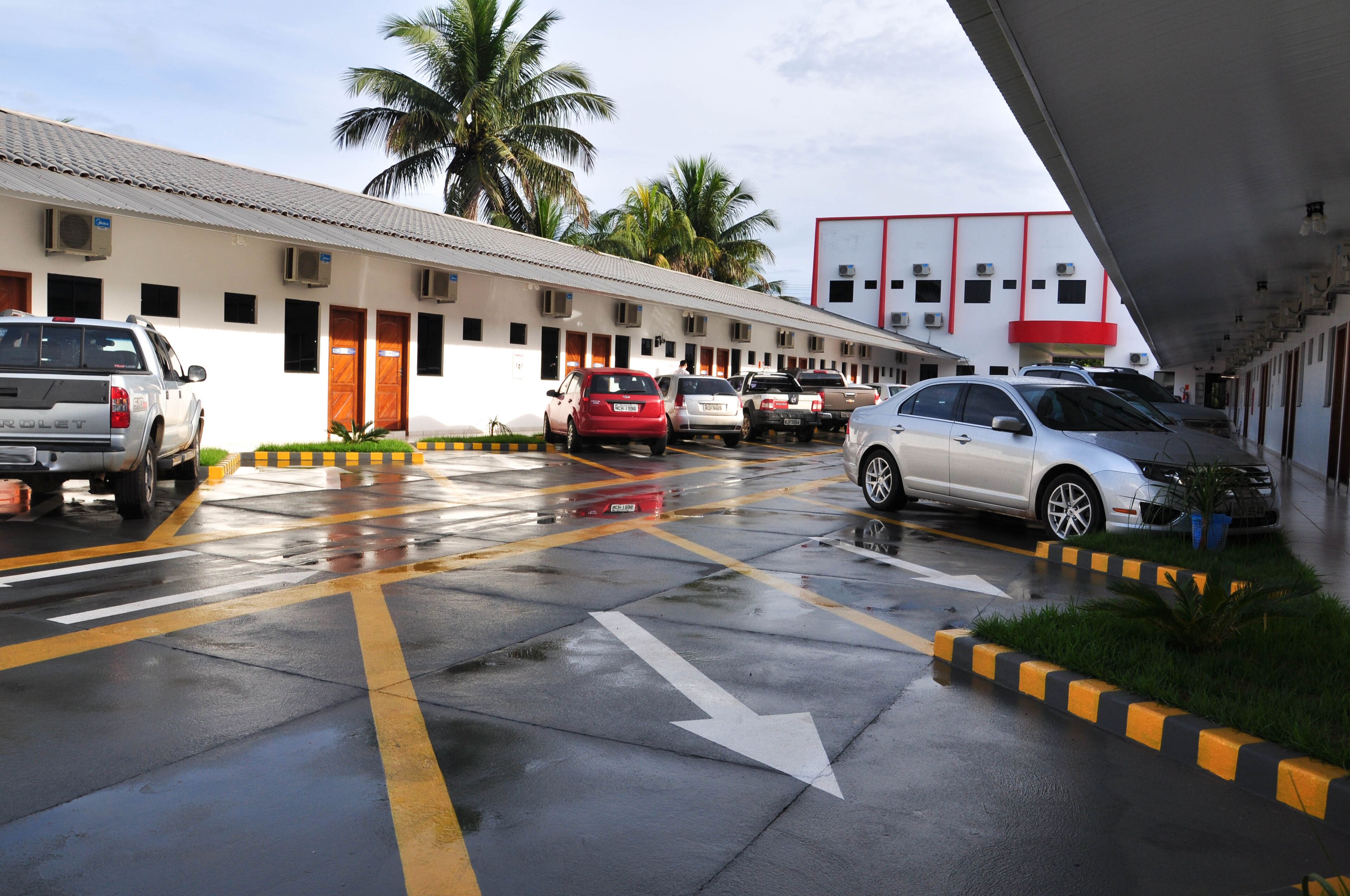 A hotel with a row of rooms, a covered parking area, and a building with air conditioning units.