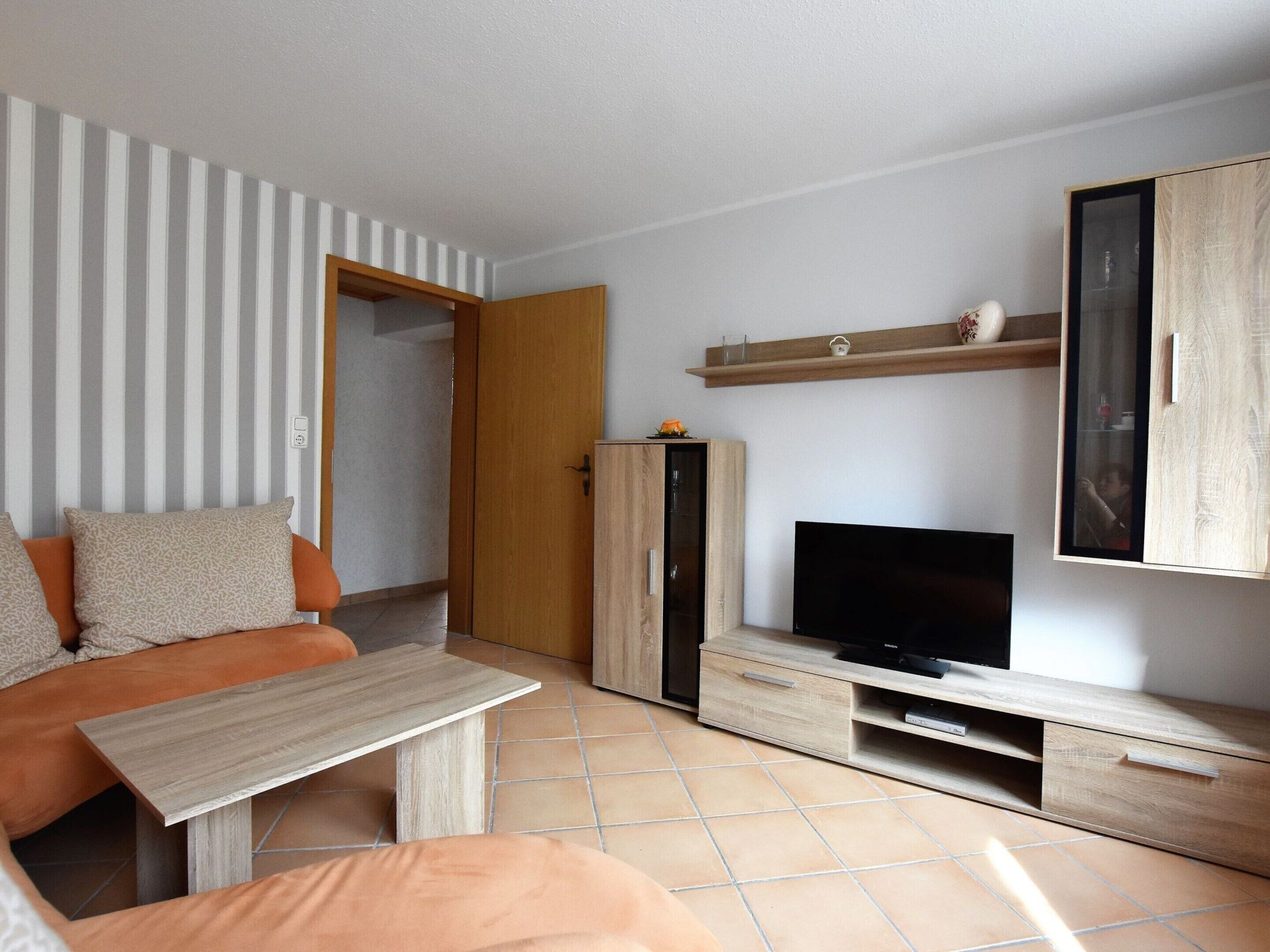 A modern living room with a sofa, TV, wooden cabinet, and tiled floor.