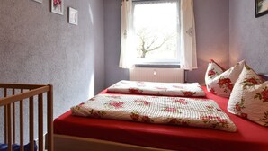 Ein Schlafzimmer mit einem hölzernen Wiege, einem Bett mit Blumenmuster-Bettwäsche und einem Fenster mit Vorhängen.