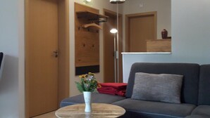 Ein modernes Wohnzimmer mit einem grauen Sofa, einem kleinen runden Tisch mit Blumen und einer Holztür.