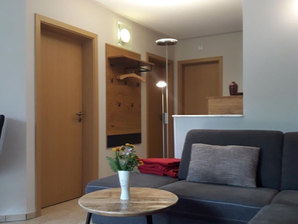 Ein modernes Wohnzimmer mit einem grauen Sofa, einem kleinen runden Tisch mit Blumen und einer Holztür.