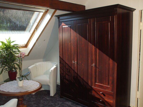 A room with a large wooden wardrobe, a white chair, a small round table with a lace tablecloth, and a potted plant. - Apartment in Bad Doberan mit Garten (Bad Doberan)
