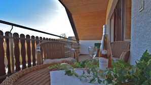 A wicker table with a bottle of wine, a glass, and a plant on a balcony with wicker chairs and a wooden ceiling. - Quiet Apartment in Merlsheim With Balcony (Nieheim)