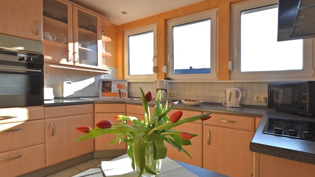 A modern kitchen with wooden cabinets, a microwave, and a vase with tulips on the counter. - Quiet Apartment in Merlsheim With Balcony (Nieheim)