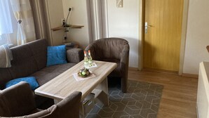 A cozy living room with a sofa, a coffee table, and a chair. There is a door and a wall with two framed pictures. - Engenstein Woodland Escape (Schleusegrund)