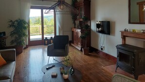 Una sala de estar con techo de madera, un sofá, una silla, un televisor, una chimenea y un balcón con vistas.