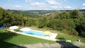 Una piscina con tobogán, rodeada de exuberante vegetación y colinas al fondo.