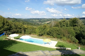A swimming pool with a slide, surrounded by lush greenery and hills in the background. - Holiday Home in Limoges With Saltwater Pool (Sussac)