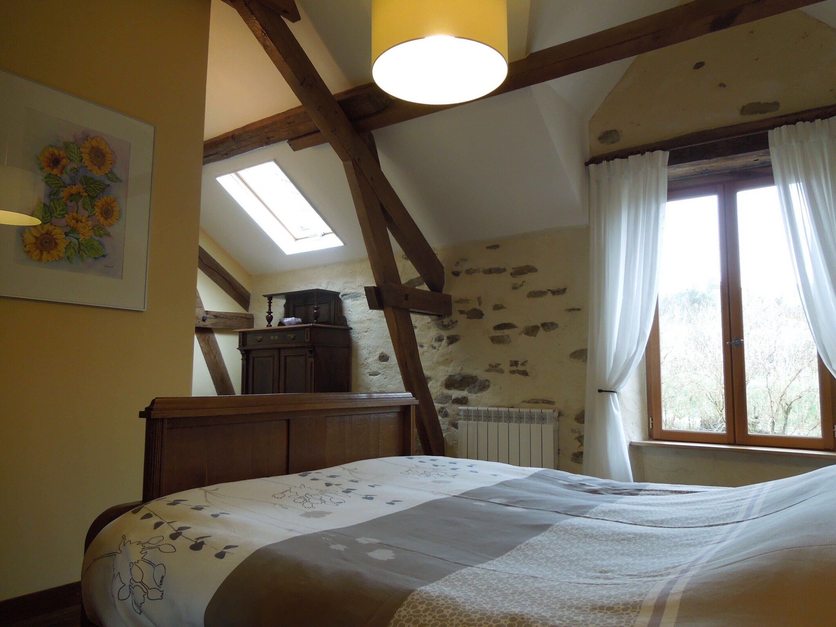 Una camera da letto con un letto, una finestra a soffitto, un termosifone e una finestra con tende.