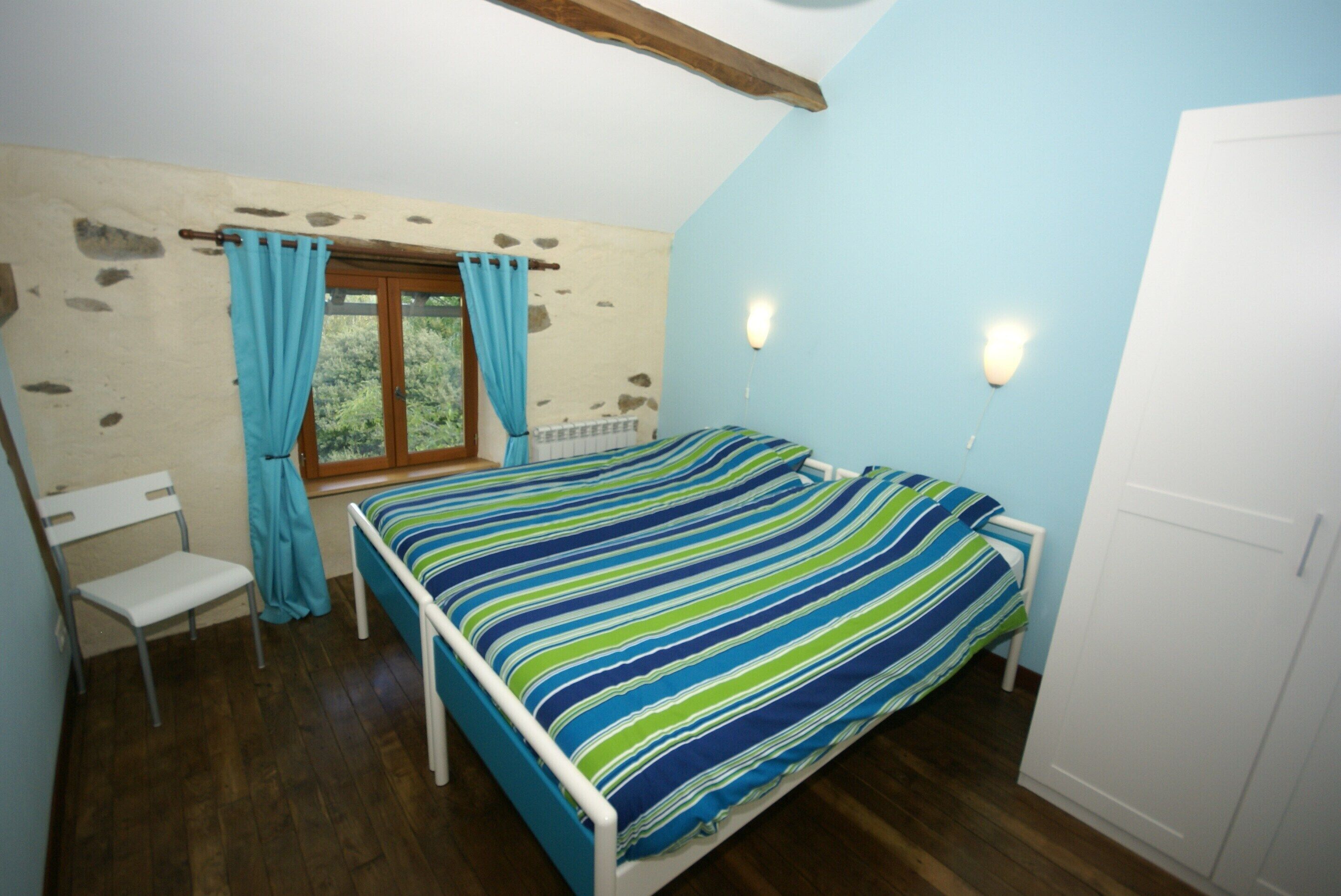 Una camera da letto con un letto, una sedia, una finestra con tende e un termosifone.