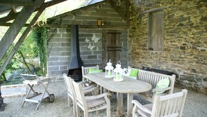 Un comedor al aire libre rústico con pared de piedra, mobiliario de madera y chimenea.