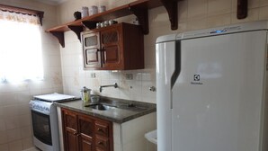 Una cocina compacta con estufa a gas, horno empotrado, pileta, armarios de madera y heladera blanca.