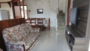Una sala de estar con un sofá floral, una mesa de comedor de madera, sillas, un televisor y una escalera que conduce a un piso superior.