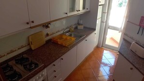 Une cuisine avec des meubles blancs, une cuisinière à gaz, un évier et une fenêtre.