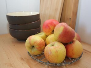 Une pile de pommes sur une table en bois, avec un bol en arrière-plan.