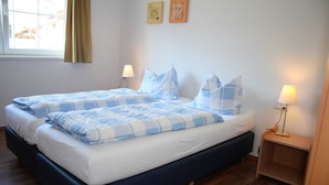 Uma cama de casal com um edredom azul e branco xadrez, duas luminárias de cabeceira e um criado-mudo de madeira.