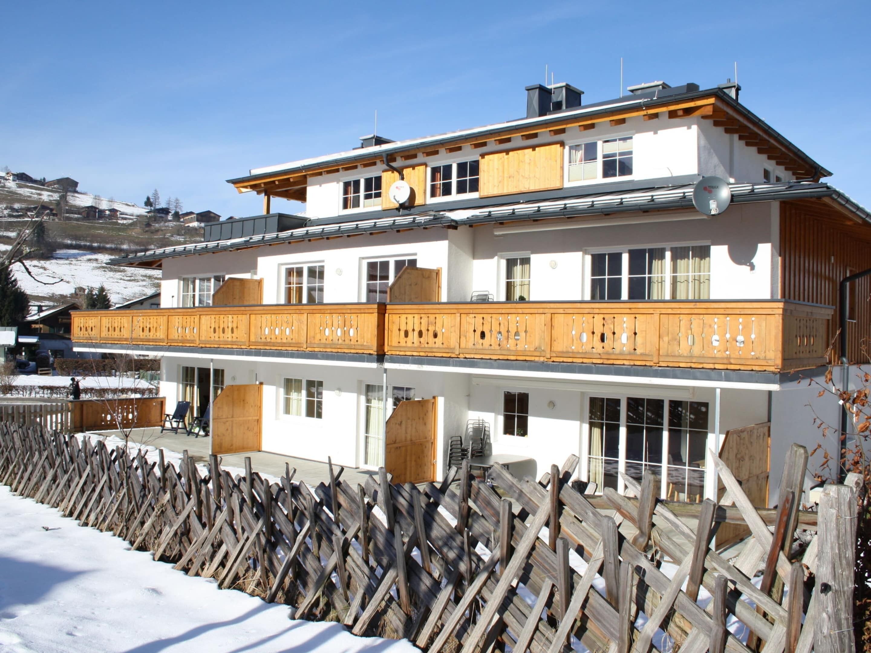 A two-story building with a wooden balcony, large windows, and a white facade.